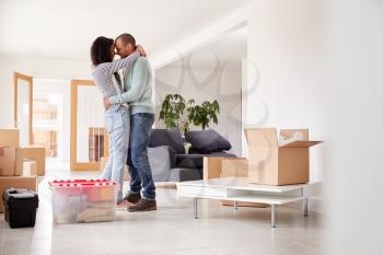 Loving Couple Hugging Surrounded By Boxes In New Home On Moving Day