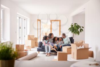 Family Taking A Break And Sitting On Sofa Celebrating Moving Into New Home Together