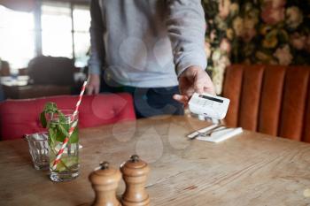 Close Up Of Waiter In Restaurant Holding Out Contactless Card Reader To Customer