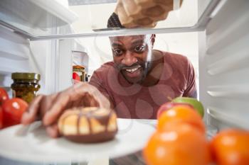 View Looking Out From Inside Of Refrigerator As Man Opens Door And Reaches For Unhealthy Donut