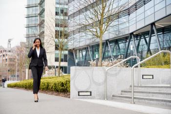 Businesswoman Commuting To Work Talking On Mobile Phone Outside Modern Office Building