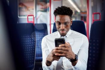 Businessman Sitting In Train Commuting To Work Checking Messages On Mobile Phone