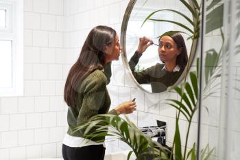Businesswoman At Home Putting On Make Up In Mirror Before Leaving For Work
