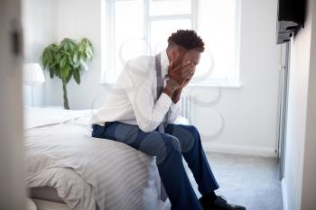 Stressed Businessman With Head In Hands Sitting On Edge Of Bed At Home