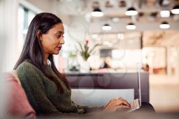 Businesswoman Sitting On Sofa Working On Laptop At Desk In Shared Workspace Office