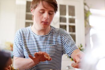 Young Downs Syndrome Man Baking Cupcakes In Kitchen At Home
