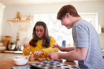 Young Downs Syndrome Couple Decorating Homemade Cupcakes With Icing In Kitchen At Home