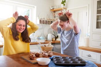 Young Downs Syndrome Couple Decorating Homemade Cupcakes With Marshmallows In Kitchen At Home