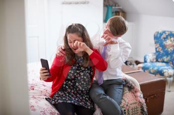 Loving Young Downs Syndrome Couple Sitting On Bed Using Mobile Phone To Take Selfie At Home