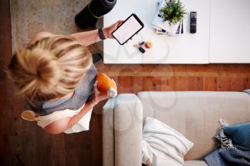 Overhead Shot Looking Down On Woman At Home Checking Phone Message Before Leaving For Fitness Class