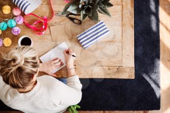 Overhead Shot Looking Down On Woman At Home Writing In Birthday Card And Wrapping Gift