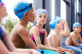 Group Of Children Sitting On Edge Of Pool Waiting For Swimming Lesson