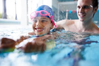 Male Swimming Coach Giving Girl Holding Float One To One Lesson In Pool