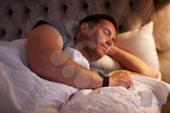 Man Sleeping In Bed Wearing Smart Watch Illuminated By Bedside Lamp