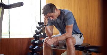 Man Anxious About Body Image Sitting On Weight Bench In Home Gym