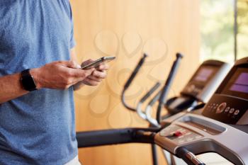 Close Up Of Man Exercising On Treadmill At Home Wearing Smart Watch Checking Mobile Phone