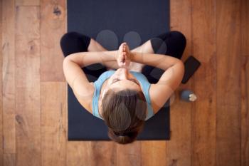 Overhead View Of Woman Sitting On Exercise Mat Wearing Wireless Earphones Connected To Mobile Phone