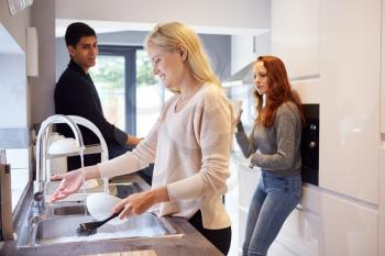 Group Of College Student Friends In Shared House Kitchen Washing Up And Hanging Out Together