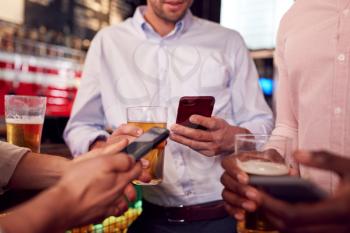 Group Of Male Friends All Checking Mobile Phones Whilst Meeting For Drink In Bar