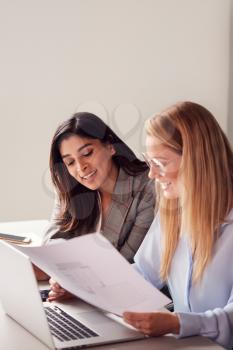 Two Young Businesswomen In Meeting Around Table In Modern Workspace Discussing Documents