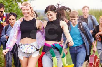 Group Of Excited Young Friends Carrying Camping Equipment Through Field To Music Festival