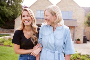 Senior Mother And Adult Daughter Walking And Talking In Garden Together