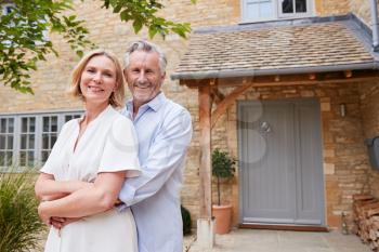 Portrait Of Senior Couple Standing Outside Front Door Of Home