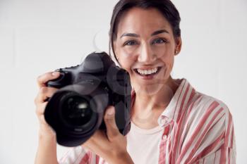 Portrait Of Smiling Female Photographer With Camera Against White Studio Wall