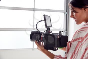 Female Videographer With Video Camera Filming Movie In White Studio