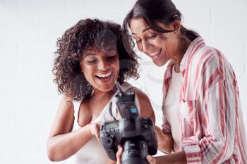 Smiling Female Photographer Holding Camera With Model In Studio Portrait Session