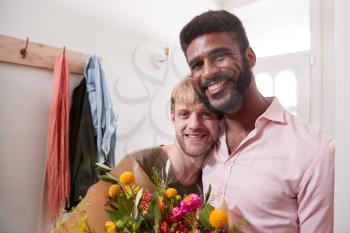 Portrait Of Man Giving Gay Partner Bunch Of Flowers In Hallway At Home