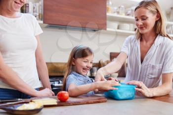 Same Sex Female Couple With Daughter Preparing School Lunchbox At Home Together