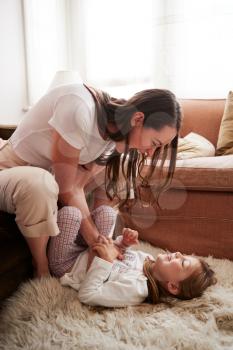 Mother Tickling Daughter As She Lies On Rug In Lounge
