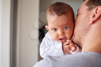 Portrait Of 3 Month Old Baby Daughter Being Held By Loving Father In Kitchen At Home