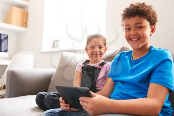 Portrait Of Brother And Sister Sitting In Lounge At Home Watching Movie On Digital Tablet Together