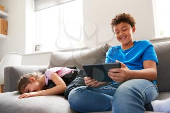 Brother And Sister Sitting In Lounge At Home Watching Movie On Digital Tablet Together