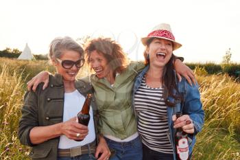 Group Of Mature Female Friends Walking Through Field On Camping Vacation Drinking Beer