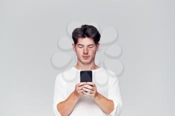 Studio Shot Of Causally Dressed Young Man Using Mobile Phone