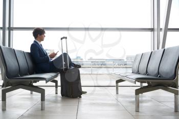 Businessman Sitting In Airport Departure Lounge Using Mobile Phone