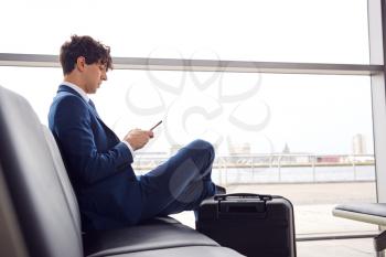 Businessman Sitting In Airport Departure Lounge Using Mobile Phone