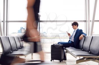 Businessman Sitting In Busy Airport Departure Lounge Using Mobile Phone