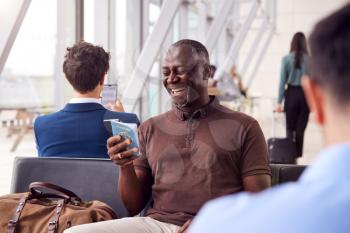 Businessman Sitting In Airport Departure Lounge Using Mobile Phone