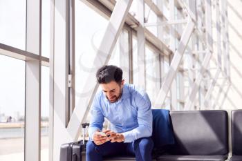 Businessman Sitting In Airport Departure Lounge Using Mobile Phone