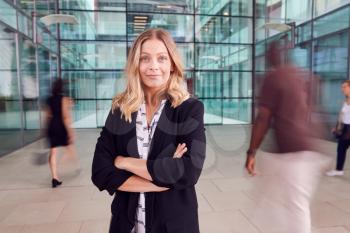 Portrait Of Businesswoman With Crossed Arms Standing In Lobby Of Busy Modern Office