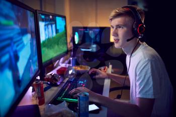 Teenage Boy Wearing Headset Gaming At Home Using Dual Computer Screens