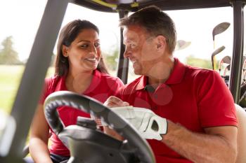 Mature Couple Playing Golf Marking Scorecard In Buggy Driving Along Course