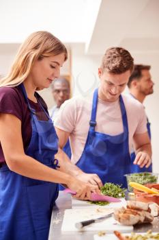 Male And Female Adult Students Preparing Ingredients For Dish In Kitchen Cookery Class