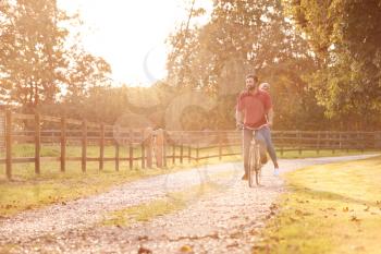 Romantic Couple Riding Bike Along Country Lane At Sunset