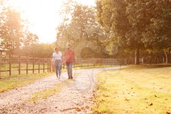 Romantic Couple Walking Hand In Hand Along Country Lane At Sunset