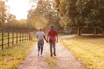 Rear View Of Romantic Couple Walking Hand In Hand Along Country Lane At Sunset